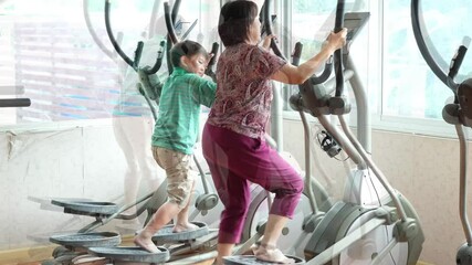 Video shows fun elliptical exercise rhythm between aunt and nephew in the gym, family activity.