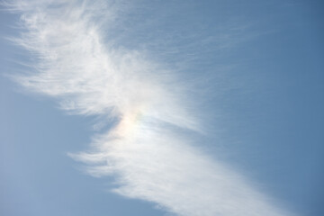 Ethereal and wispy white clouds with faint cloud bow from backlit sun against a blue sky, as a...