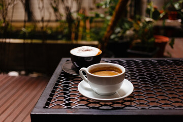 Cappuccino with cinnamon and a cup of hot black coffee on the table. Delicious invigorating coffee for breakfast