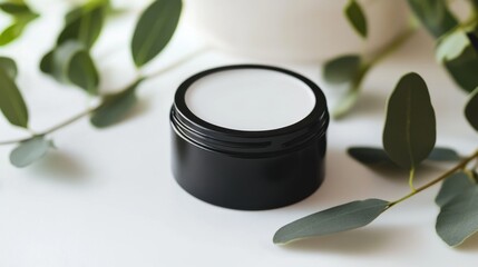 A sleek black cosmetic jar rests on a clean surface, surrounded by eucalyptus leaves, creating a serene and elegant beauty scene, perfect for skincare branding.