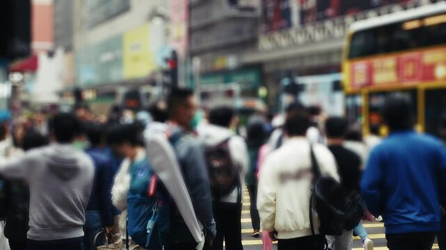 Crowded pedestrian intersection in Hong Kong, featuring people crossing the street, urban buses, and vibrant cityscape. Dynamic street life captures the essence of city living