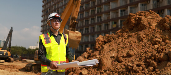 Civil engineer or site construction engineer with safety PPE, holding drawings, working on site