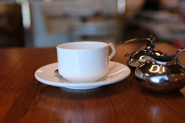 tea time elegance, a white teacup filled with tea sits on a saucer with a spoon, next to a teapot...