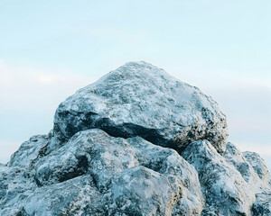 Serene stack of large, grey boulders against a soft, light blue sky; minimalist nature scene.