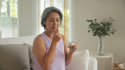 Asia adult aged people middle age happy old woman smile drink vitamin d c e k zinc omega 3 fish oil water pill reduce hot flash dry skin health care sit at home sofa elder aging asian. Take diet food.