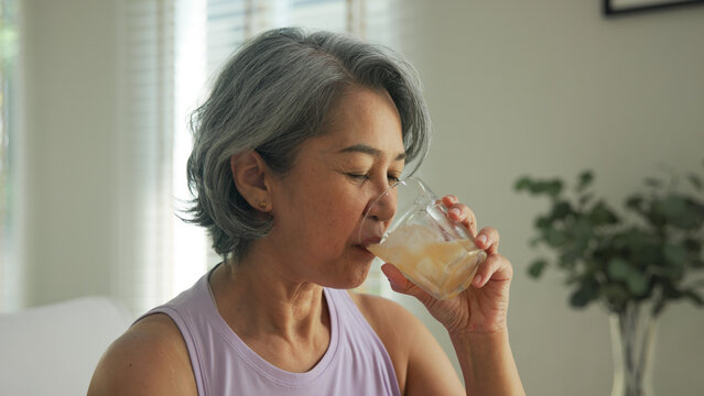 Asia adult people middle age happy old woman pour weight loss tea fiber juice drink kombucha gut health care diet detox sit at home sofa elder aging asian aged female. Fresh bottle medical food relief