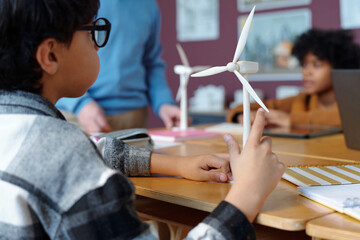 School children engaging in hands-on learning about renewable energy sources using wind turbine models in science classroom with teacher offering guidance on sustainability concepts