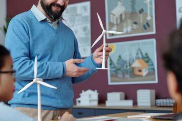 Smiling teacher explaining wind energy model to students in classroom, engaging them with hands-on activities for renewable energy education