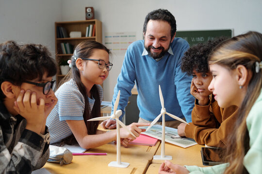 Educator discussing wind turbines with diverse students in classroom creating engaging learning environment focused on renewable energy sources