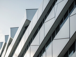Abstract view of a modern building facade with geometric white panels and dark windows against a light sky.
