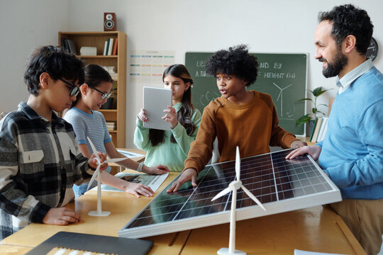 Group of diverse children and teacher working in classroom on solar energy project with wind turbines, discussing and collaborating on renewable energy concepts