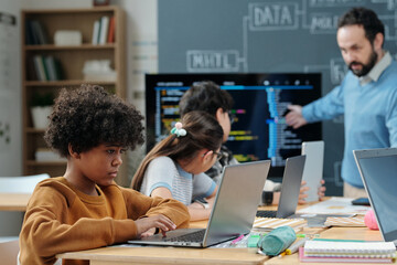 Diverse group of children engaging in a classroom session with laptops while teacher explaining...