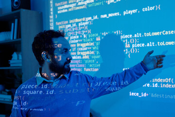 Business professional presenting data analysis on digital screen in dark room. Engaging in technology-driven environment with complex code projections behind him