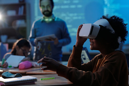 Students experiencing virtual reality technology in classroom while engaging with immersive educational content. Teacher observing and assisting with demonstrations