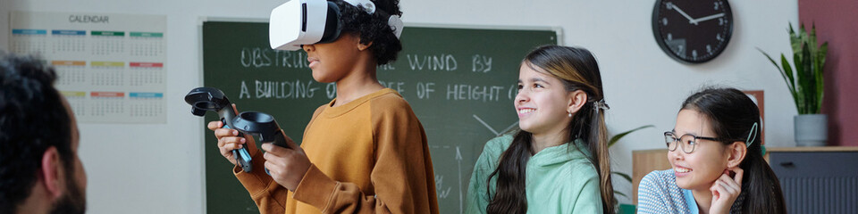 Multiracial group of students experiencing virtual reality technology in classroom environment, exploring virtual world, interacting with devices and learning in modern, engaging way