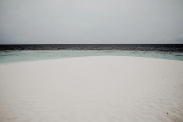 Obraz premium 灰色の空の下、穏やかな波が打ち寄せる白い砂浜が広がるビーチ。