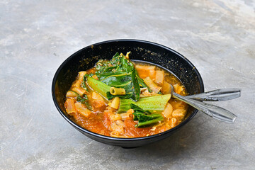 Close up view of seblak in the black bowl, grey or gray cement as background. This is a spicy culinary dish from West Java containing crackers and various aci with the main spice kencur.