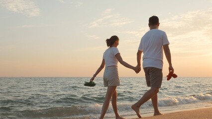 Vacation loving couple walking on beach together at sunset landscape, relaxing vacation travel summer, Asian man and woman in love holding hands walks along the sandy seashore