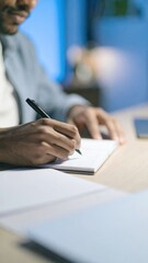A person is writing in a notebook with a pen, focused on their task, surrounded by a minimalistic workspace.