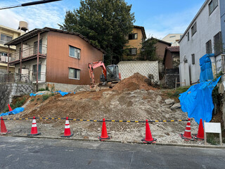 small construction site in a residential Japanese neighborhood - building a house on a plot of land - construction equipment machinery, traffic cones, tarp, houses, apartment, street - Nagoya, Japan