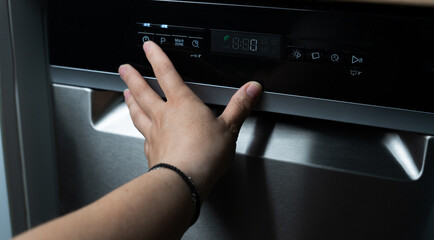 Hand selecting dishwasher program on control panel, modern kitchen appliance. Built-in appliances...