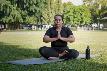 Mindful Asian woman wearing sportswear doing yoga meditation pose, sitting in lotus position at...