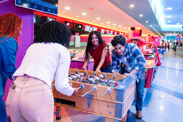Group of happy young friends playing table football in a bowling alley and arcade video game room