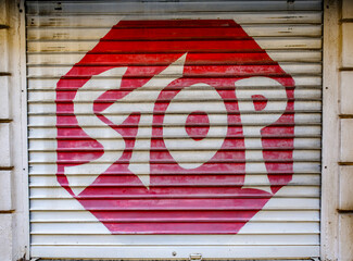 Stop sign painted on a shop shutter in an urban setting during daylight hours, showcasing a creative take on a familiar traffic symbol