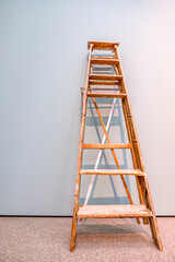 Rustic wooden ladder positioned against a light blue wall in an indoor space during daylight hours