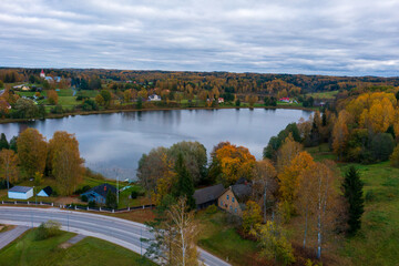 Fototapeta premium Aerial view of Rõuge lake surrounded by vibrant autumn foliage in the Estonian countryside. Rural village with scattered houses along the shoreline under cloudy skies revealing the beauty of Estonia