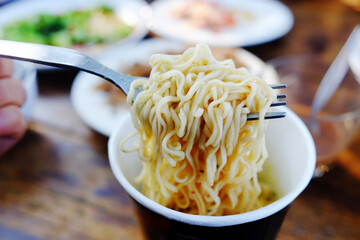 Hand holding fork with fresh noodles served in a cup in the morning