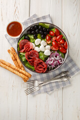 Pizza salad tosses mix of romaine lettuce, sausages, mozzarella, black olives and red onion in a fresh, grated tomato vinaigrette closeup on the plate on the wooden table. Vertical top view from above