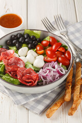 Pizza salad with sausages, mozzarella balls, tomatoes, olives, onions, romaine lettuce and spicy vinaigrette dressing close-up in a bowl on the table. Vertical