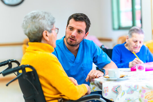 Male nurse assisting elderly woman in wheelchair at nursing home