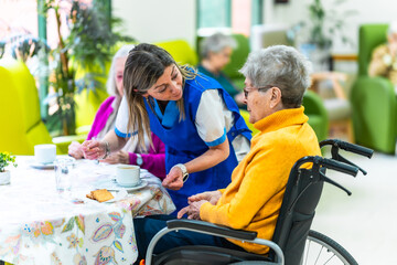 Nurse assisting elderly woman in wheelchair at nursing home during lunch break