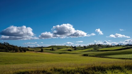 Obraz premium Breathtaking landscape showcasing rolling hills under a bright blue sky with fluffy white clouds.