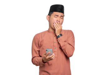 Confused young Asian Muslim man holding mobile phone and feeling sleepy isolated on transparent background