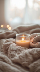 Soft glowing candle resting on a cozy knitted blanket, warm morning light creating a peaceful and serene atmosphere indoors.