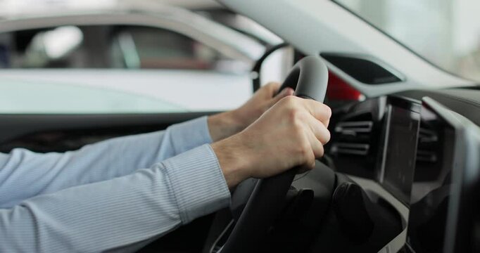 Close up young man auto driver car owner holding steering wheel buy new automobile dealership inside vehicle. Concept of car shopping, buying, and dealership.