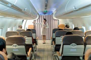 Flight attendant pointing to the emergency exit during pre-flight safety demonstration inside airplane cabin, ensuring passengers are informed and prepared