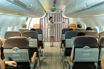 Flight attendant giving safety instructions to passengers by pointing toward emergency exits during...