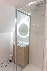 Salle de bain moderne avec douche vitrée et miroir rond, combinant esthétisme minimaliste et fonctionnalité contemporaine.