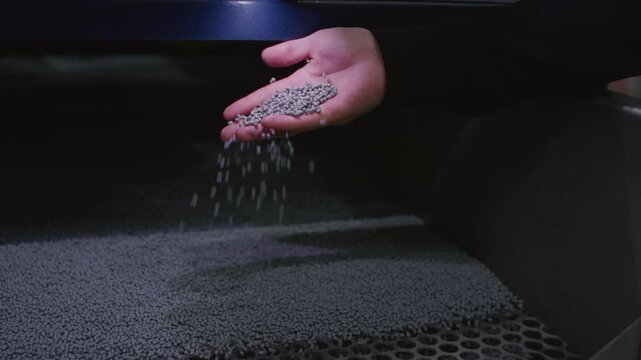 The hand touches the microplastic granules from the extruder. Plastic or polypropylene pellets on the conveyor belt of the machine. The engineer checks or inspects the raw materials for processing.