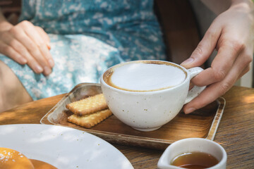 Enjoying a warm cup of coffee with biscuits in a cozy cafe during a sunny afternoon Cappuccino mug in a woman's hand on a wooden table, morning coffee.