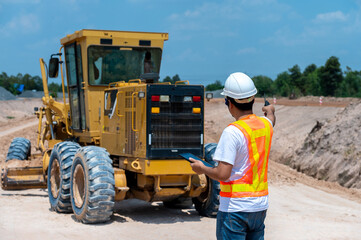 Construction Worker Operating Grader: A construction worker in a safety vest and helmet operates a large yellow grader, skillfully maneuvering the machine on a construction site.