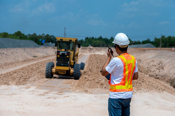 Construction Site Supervisor: A construction supervisor with a radio in hand oversees a massive...