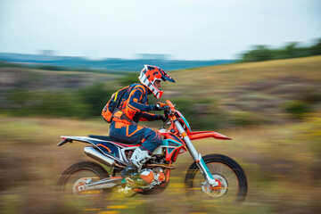 Side view of a motocross rider speeding across a grassy field with motion blur background, emphasizing speed and dynamic movement. Off-road racing in nature