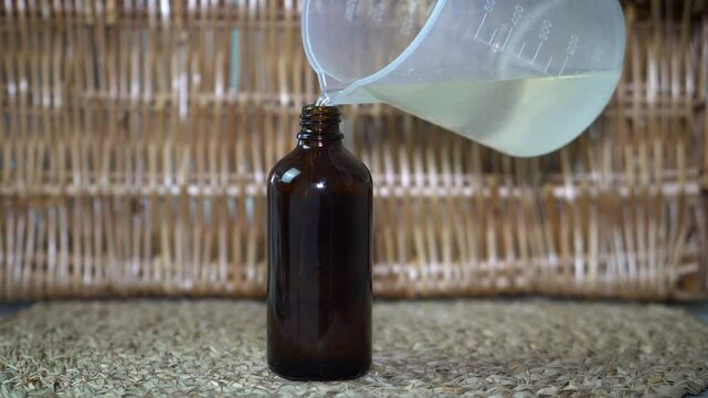 Woman pouring natural homemade skin toner into amber glass spray bottle on beige background. DIY organic skincare, clean beauty, and self-care preparation in warm, minimal setting.