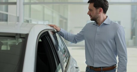 Portrait of handsome man touching new car in showroom. Concept of car shopping, buying, and dealership.