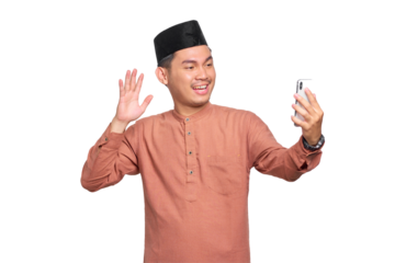 Cheerful young Asian Muslim man doing selfie shot on mobile phone waving hand isolated on transparent background